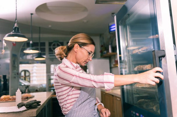 Owner of French bakery wearing glasses looking at fridge with desserts - Фото, изображение
