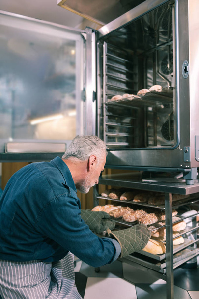 Owner of bakery putting croissants into oven working in the morning - Fotoğraf, Görsel