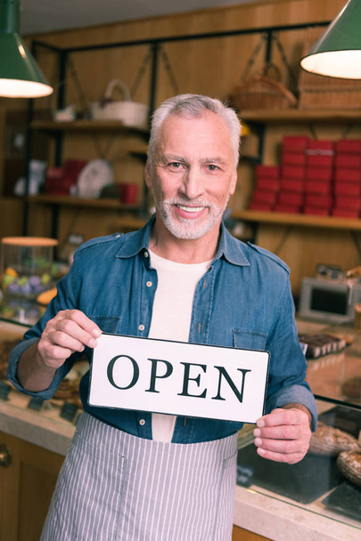 Smiling grey-haired businessman wearing denim shirt opening his cafeteria - Foto, Bild