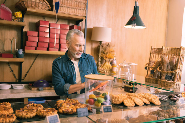 Bearded grey-haired owner of bakery selling cookies in the morning - Zdjęcie, obraz