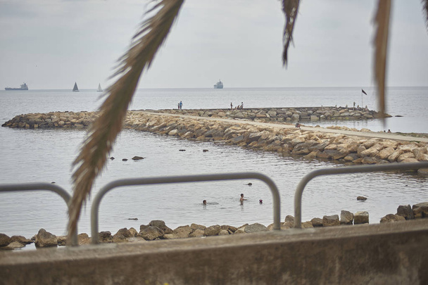 Pier de rochas no mar Mediterrâneo filtrado por um parapeito com navios em movimento no horizonte
. - Foto, Imagem