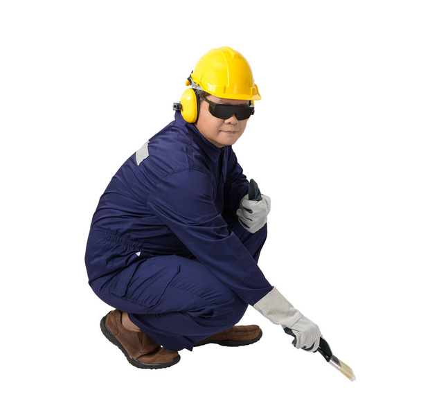Работник в механическом комбинезоне Сидя и держа кисть с шлемом, наушники, защитные перчатки и защитные очки изолированы на белом фоне обрезки пути
 - Фото, изображение