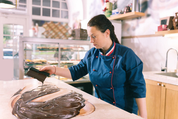 Dark-haired female chef feeling inspired cooking tempered chocolate - Foto, Imagen