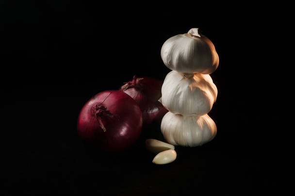Σύνθεση των δύο κόκκινα κρεμμύδια και τρία κεφάλια σκόρδο σε μαύρο φόντο - Φωτογραφία, εικόνα