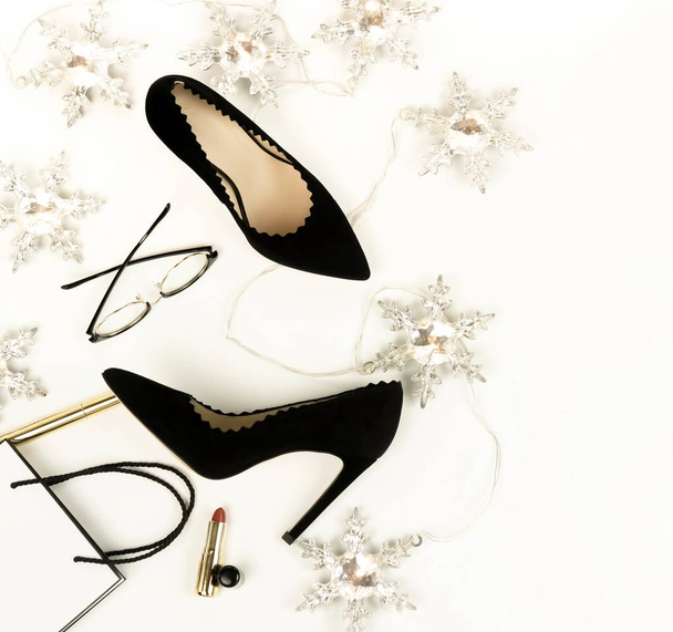 Women's black high heels shoes and accessories glasses, cosmetics, lipstick, bag, Christmas garland top view on a white background.  Holiday fashion concept. Flat lay.  - Fotoğraf, Görsel