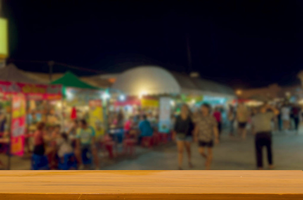 wood top table blurred people walking at night market walking street. Can be used for display or montage your products. - Foto, Imagem