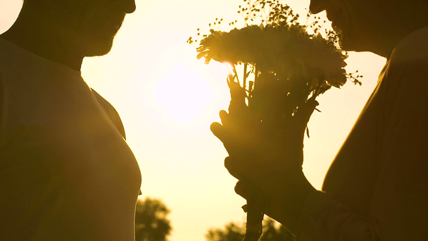 Hombre dando flores a la mujer y se besan en el fondo del atardecer, momento romántico
 - Metraje, vídeo