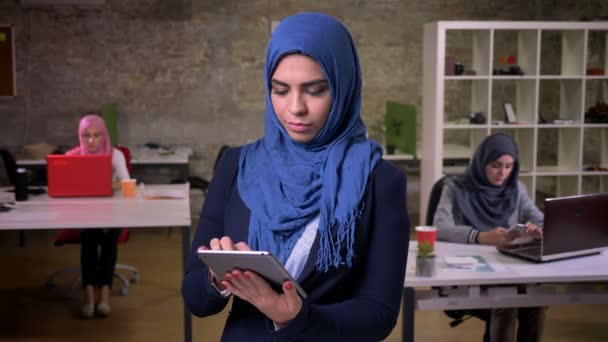 Beautiful smile of arabic female who shows green screen on tablet and stands in brick office among her arabian colleagues, indoor illustration, modern life - Materiaali, video
