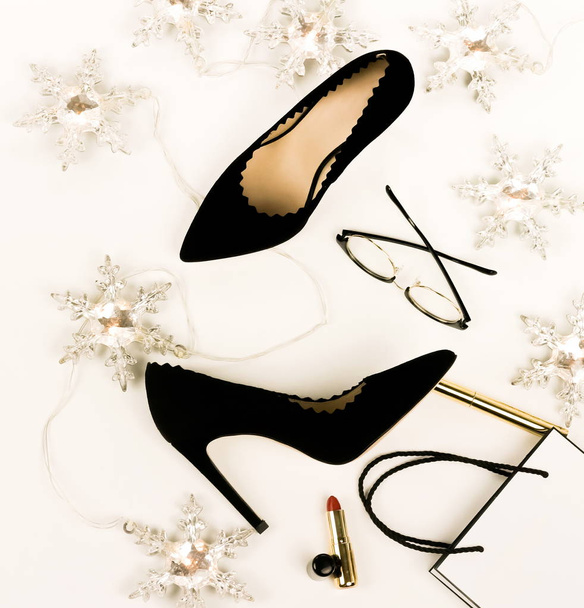 Women's black high heels shoes and accessories glasses, cosmetics, lipstick, bag, Christmas garland top view on a white background.  Holiday fashion concept. Flat lay.  - Valokuva, kuva