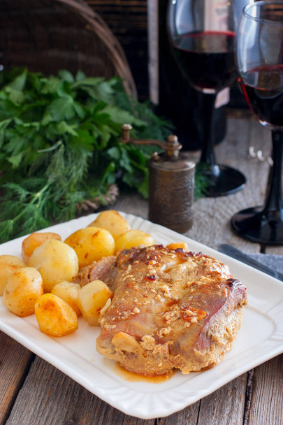 Baked turkey thigh meat with potatoes on a wooden table and glasses of red wine, selective focus - Photo, Image