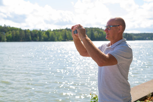 Gelukkig Senior Man nemen van foto met de telefoon bij het meer - Foto, afbeelding