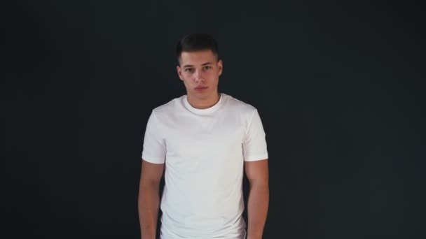 Portret van aantrekkelijke en knappe jonge man in een wit overhemd staat en ziet er op de camera. Geïsoleerd op zwarte achtergrond - Video