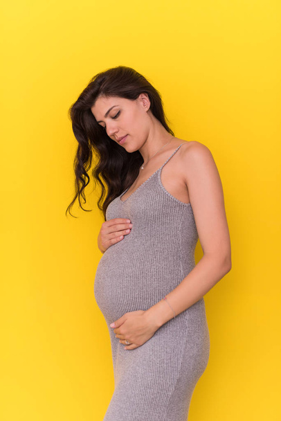 Portrait of happy pregnant woman with hands on belly isolated over yellow background - Фото, зображення