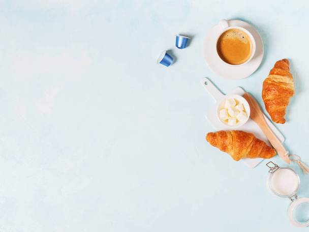Cup of coffee with capsules, croissants and butter on blue pastel background - Фото, изображение