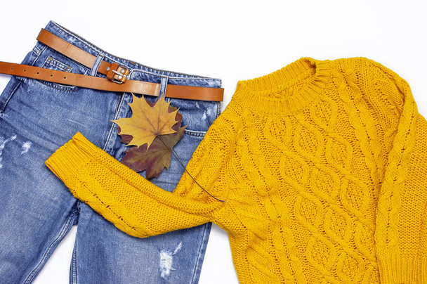 Female orange knitted sweater, blue jeans and autumn leaves on white background top view flat lay. Fashion Lady Clothes Set Trendy Cozy Knit Jumper Autumn accessories Female fashion look - Zdjęcie, obraz