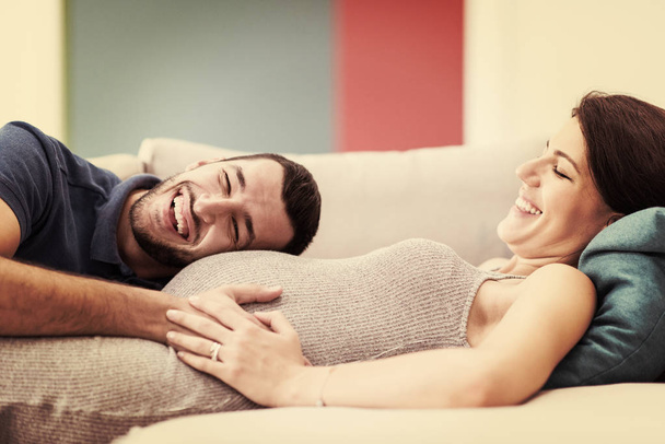 Happy future dad listening the belly of his pregnant wife while relaxing on sofa at home - Φωτογραφία, εικόνα