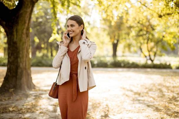 Gelukkig jonge vrouw met behulp van mobiele telefoon in de herfst park op mooie dag - Foto, afbeelding