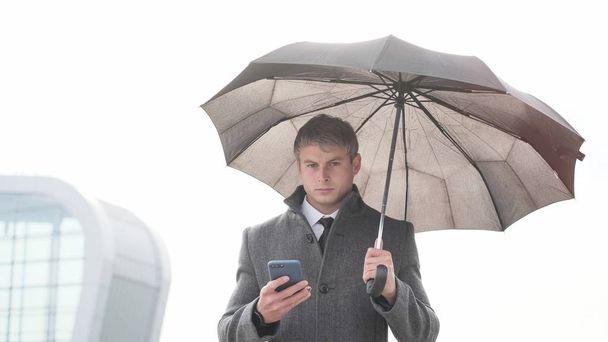 Portrait of handsome business man using smartphone. Young businessman holding umbrella and using a smart phone in a rainy day. - Foto, Bild