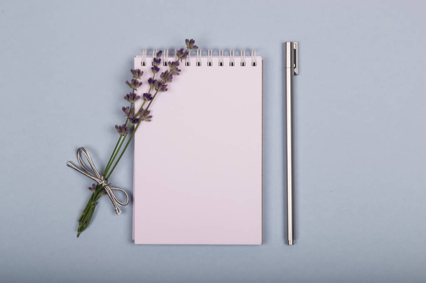Bloc de notas blanco sobre un fondo azul con un pequeño ramo de lavanda púrpura y un bolígrafo de plata acostado en él
. - Foto, imagen