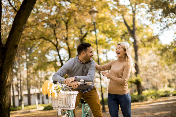Active young couple enjoying together in romantic walk with bicycle in golden autumn park - Photo, Image
