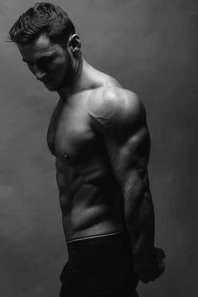 Zwart-wit dicht omhoog portret van fitness atletische jongen tonen van spieren. Bodybuilding. Sterke man die zich voordeed op achtergrond. - Foto, afbeelding