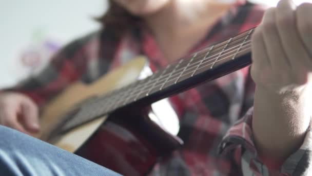 Ένα κορίτσι σε ένα καρό πουκάμισο που μαθαίνει να παίζει κιθάρα - Πλάνα, βίντεο