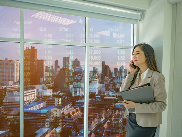 Modern üzleti nők használata mobiltelefon beszélni tőzsdei fehér néz ki az ablakon, az irodájába, városkép állomány száma, üzleti klara - Fotó, kép
