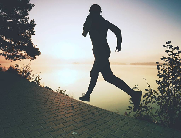 Πάγωμα βολή δράση του ψηλός αθλητής τρέχει φοράει μοντέρνα παπούτσια για τρέξιμο και αθλητικά ρούχα άσκηση το πρωί στην ακτή. Πεζοδρόμιο τροχιά γύρω από τη λίμνη. - Φωτογραφία, εικόνα