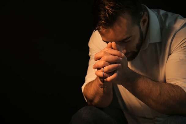 Religious young man praying to God on black background - Photo, Image