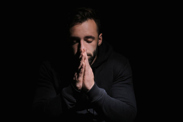 Religious young man praying to God on black background - Photo, Image