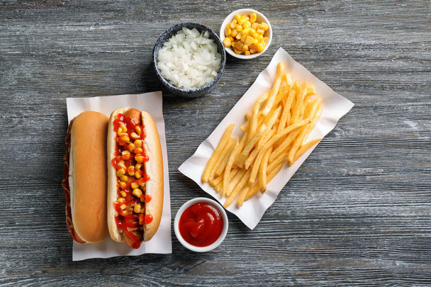 Tasty hot dogs with corn, cut onion and french fries on wooden table - Photo, Image