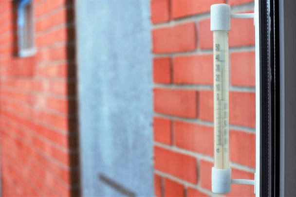 The outside temperature of the thermometer is made of plastic, hanging on the window. Background red brick building wall - Foto, Imagem