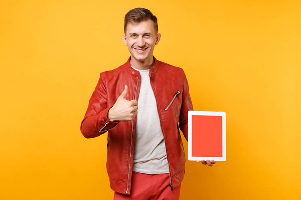 Portret vogue leuke jongeman in rood lederen jas t-shirt greep tablet pc pad met lege leeg scherm geïsoleerd op heldere gele achtergrond. Mensen oprechte emoties levensstijl concept. Gebied van de reclame - Foto, afbeelding