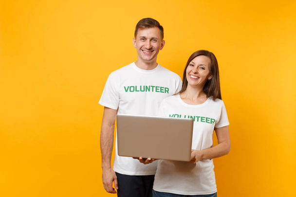 Colleagues couple in white t-shirt with inscription green volunteer using typing laptop pc computer isolated on yellow background. Voluntary free work, assistance help, charity grace teamwork concept - Photo, Image