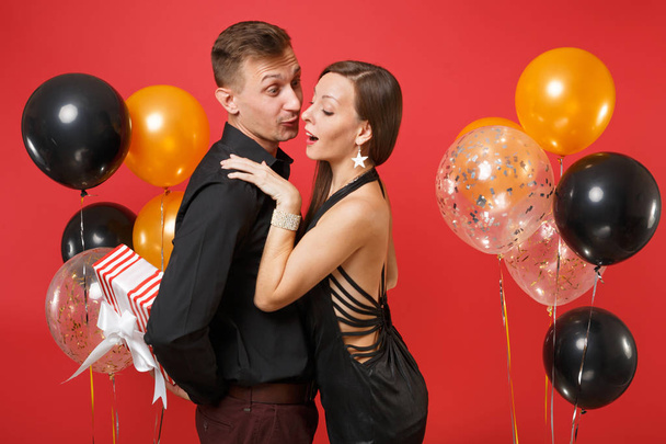 Young couple in black clothes hold gift box celebrating birthday holiday party isolated on bright red background air balloons St. Valentine International Women Day Happy New Year 2019 concept. - Φωτογραφία, εικόνα