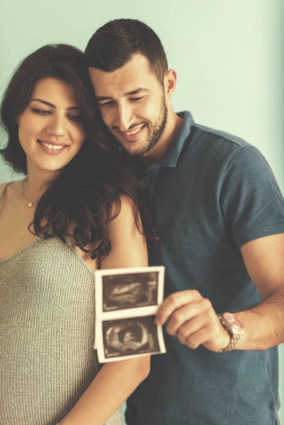 happy pregnant couple looking ultrasound picture of their unborn baby, isolated on blue background - Foto, afbeelding