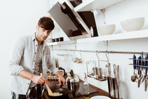 Selektywny fokus młody człowiek gotowanie jajecznica na piecu w kuchni  - Zdjęcie, obraz