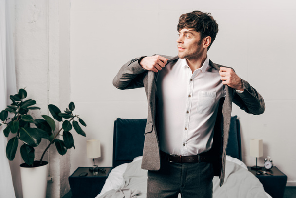 side view of handsome businessman putting on jacket in bedroom at home - Foto, immagini