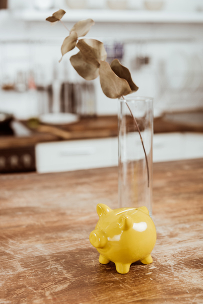 selective focus of branch in vase and piggy bank at wooden table  - Foto, Bild