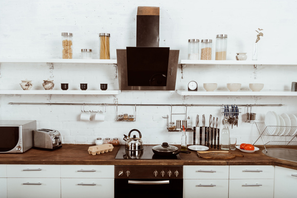 selective focus of modern kitchen interior with frying pan and teapot on stove  - Fotó, kép
