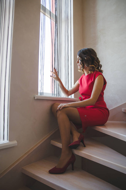 Attractive young woman in red dress sitting on stairs  - Photo, Image
