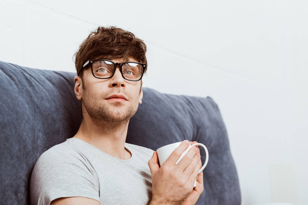 красивий молодий чоловік в окулярах з чашкою кави вдома
 - Фото, зображення