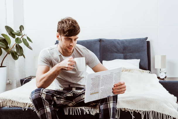 συμπυκνωμένο νεαρός άνδρας διαβάζει εφημερίδα και να πίνει καφέ στο σπίτι - Φωτογραφία, εικόνα