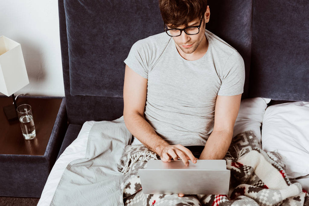 high angle view of male freelancer working on laptop in bed at home - Foto, immagini