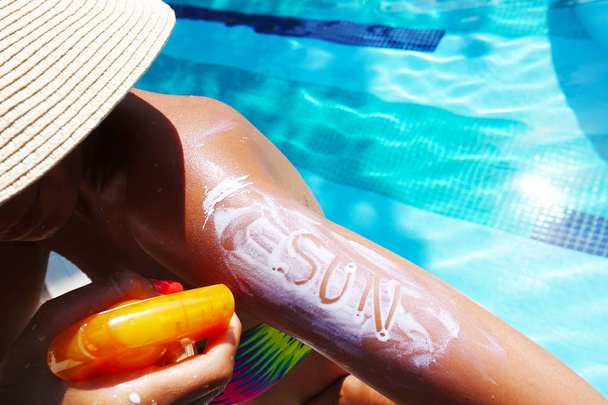 Texto de sol sobre protector solar aplicado con spray en brazo de mujer junto a la piscina
 - Foto, imagen