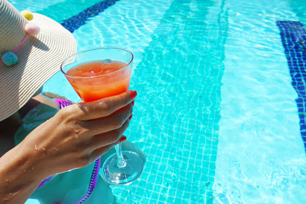 Giovane donna con cappello e costume da bagno colorato bere cocktail in piscina
 - Foto, immagini