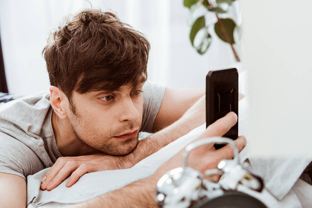 enfoque selectivo del hombre usando el teléfono inteligente mientras está acostado en la cama en casa
 - Foto, imagen