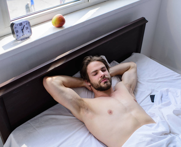 Pleasant relax concept. Let your body feel comfortable. Man unshaven handsome guy naked torso relaxing bed. Guy sexy macho lay white bedclothes. Man sleepy drowsy unshaven bearded face having rest - Фото, зображення