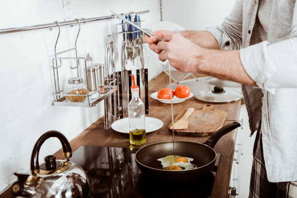 visão parcial do jovem cozinhando ovos mexidos no café da manhã na cozinha
  - Foto, Imagem