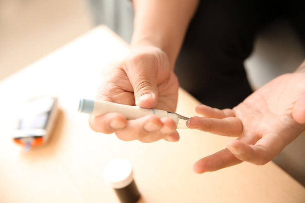 Diabetic man taking blood sample with lancet pen at home, closeup - Photo, Image